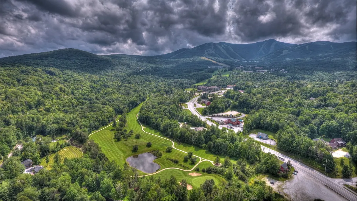 A panoramic landscape reveals rolling mountains, a winding road, a serene golf course, a reflective pond, and a dense forest. The scene captures the breadth of outdoor activities available in Killington, from golfing to hiking and scenic drives.