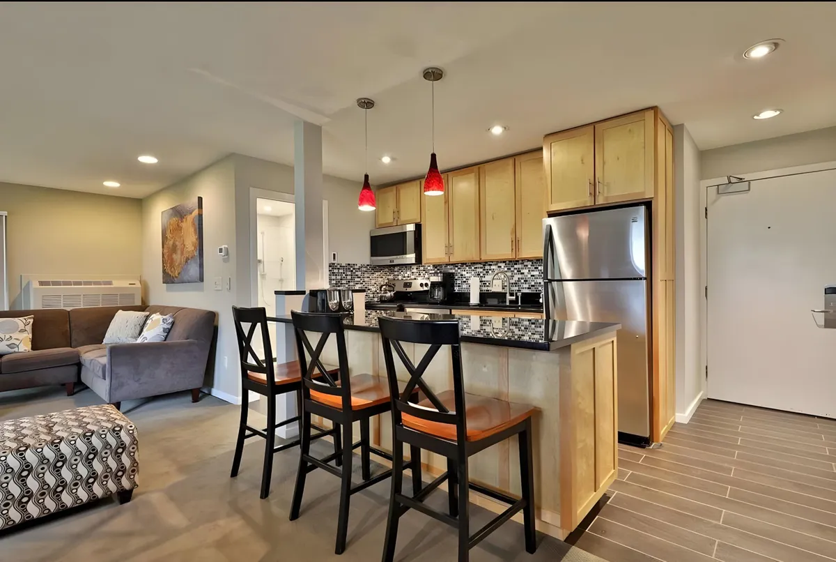 A cozy interior with a kitchen island surrounded by bar stools, adjacent to a plush sofa and a decorative ottoman. The setup encourages socializing, casual dining, and group gatherings after a day exploring local nightlife.