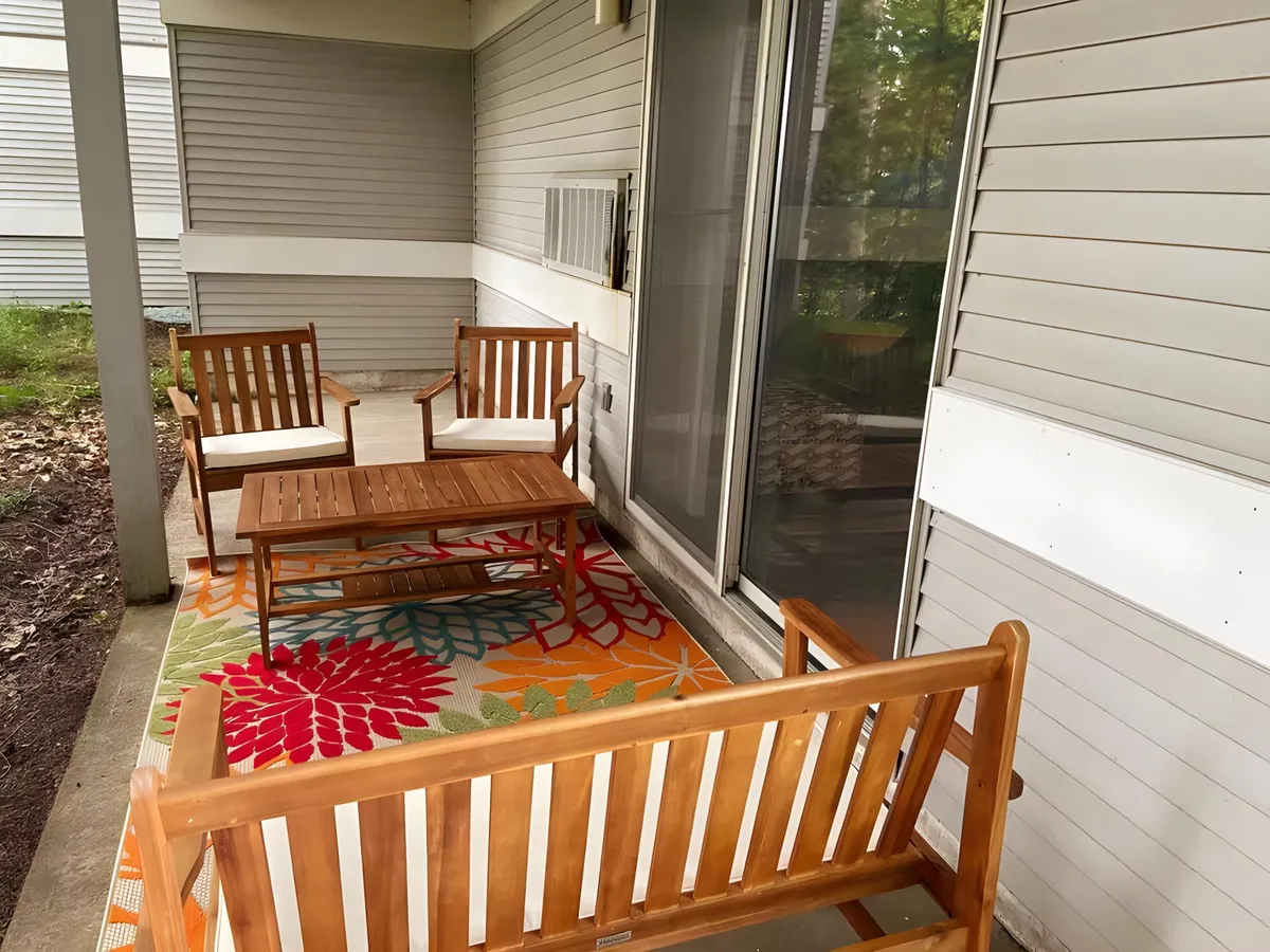 An exterior scene showcasing wooden seating arranged around a colorful rug and coffee table, inviting guests to relax or socialize outdoors. The warm wash of sunset or morning light creates a cozy, welcoming atmosphere and suggests the ease of transitioning between indoor comfort and outdoor adventure.