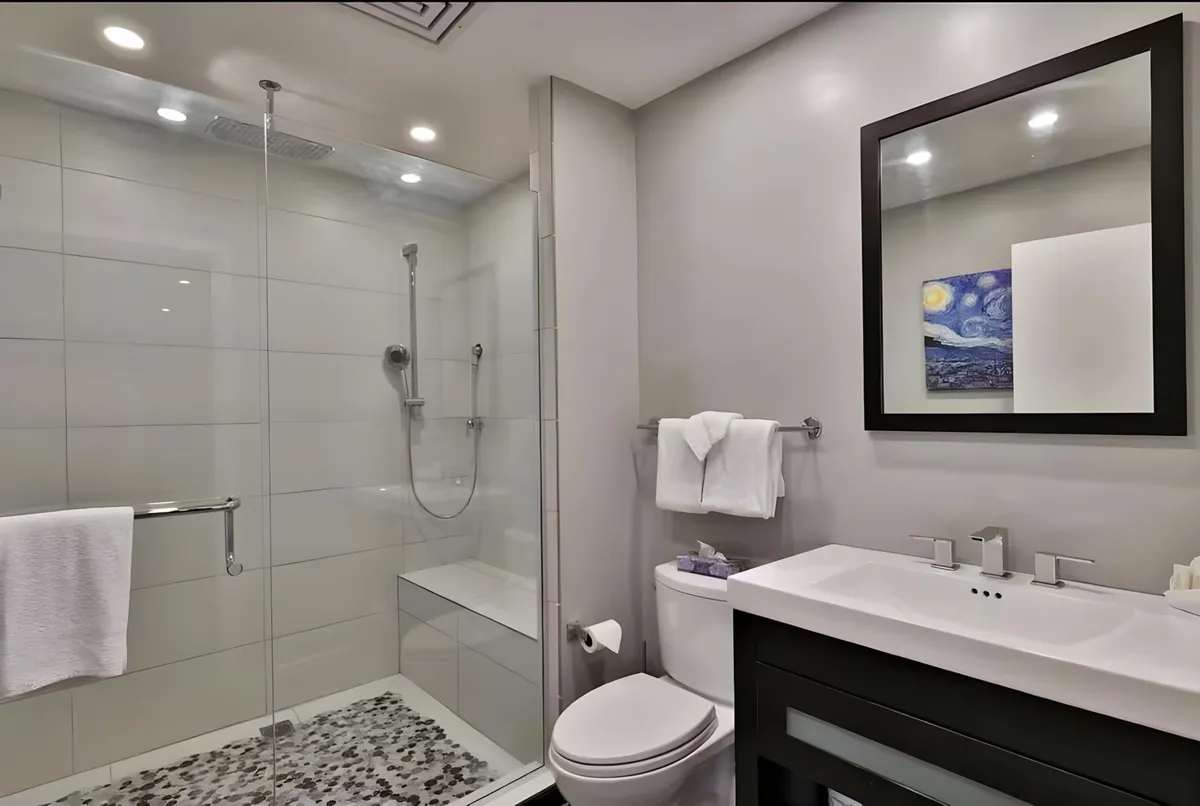 A modern bathroom featuring a glass shower enclosure, a well-lit sink area with a contemporary faucet, and decorative wall art. The space feels clean, inviting, and convenient for guests needing a comfortable refresh after a day outdoors.
