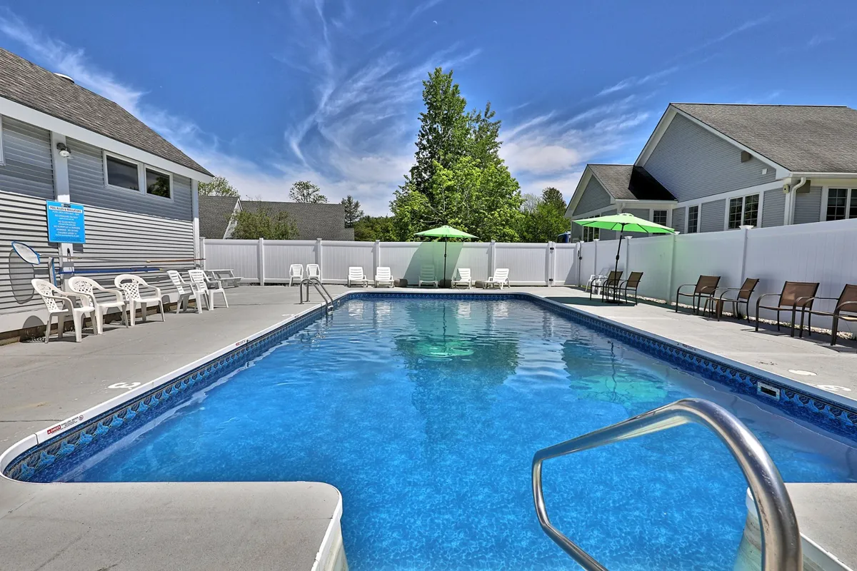 A spacious outdoor heated saltwater pool surrounded by comfortable lounge chairs and vibrant green umbrellas, set among tall, leafy trees. Guests are seen swimming, sunbathing, and socializing, creating a lively, resort-style atmosphere.