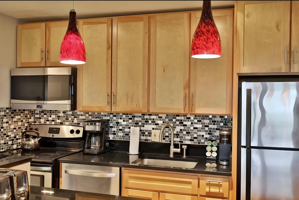 A stylish kitchen with red pendant lights, a sleek black countertop, a vibrant mosaic backsplash, and stainless steel appliances. The atmosphere is both contemporary and warm, hinting at enjoyable cooking and dining experiences.